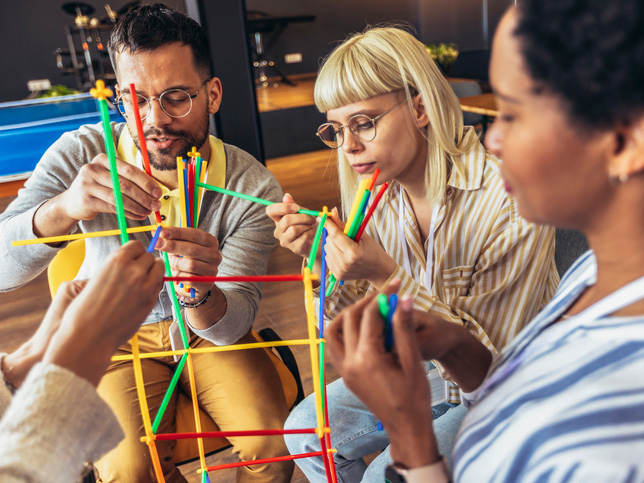 Diverse team members doing a team building activity in the office with sticks.