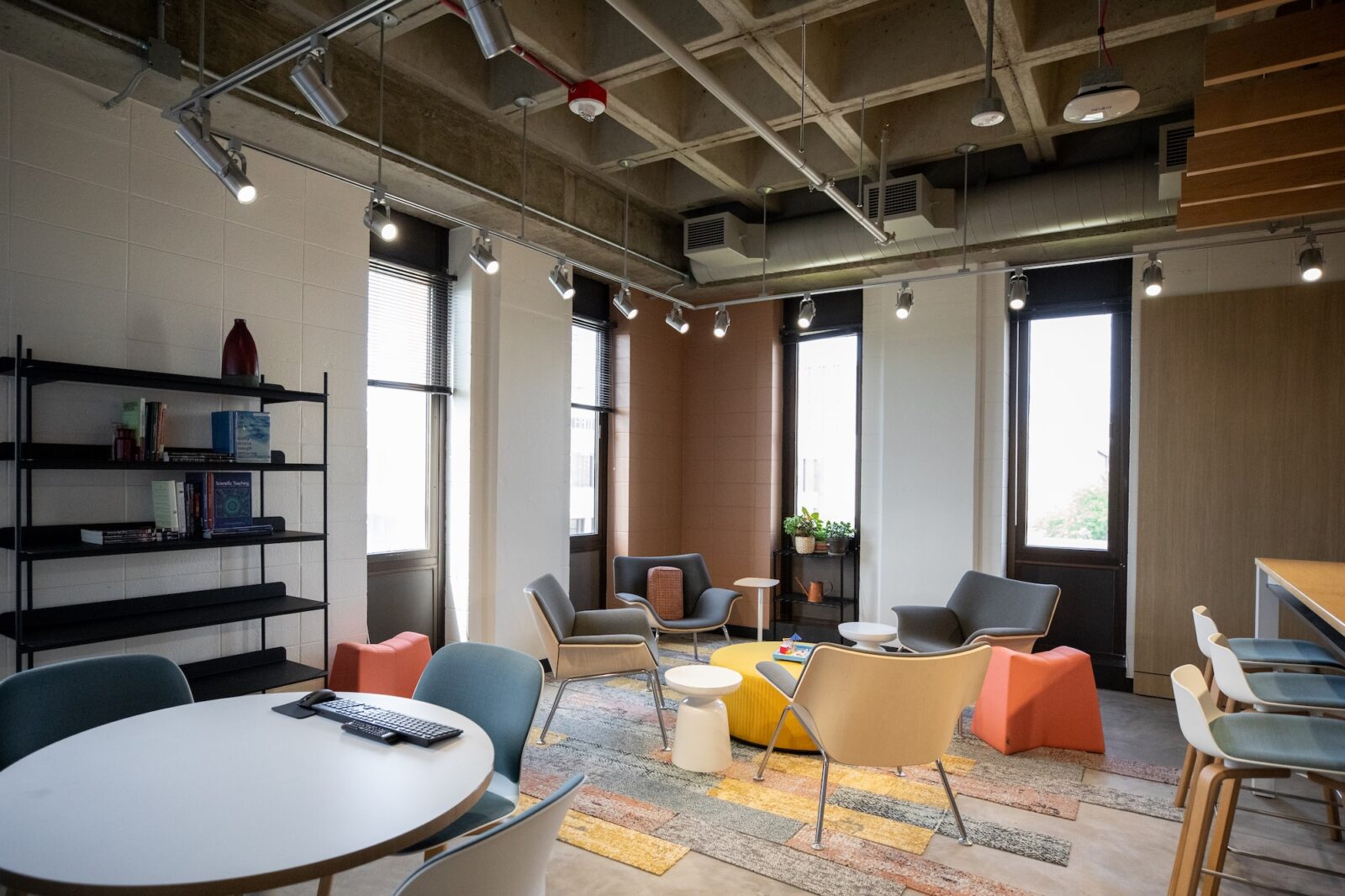 Empty room that has a round table, bookshelf, and chairs that are in a circle together in it.